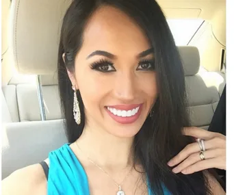 Close-up of a woman smiling in a car, wearing large earrings and a blue top.