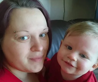 Mother and baby smiling while sitting on a couch indoors.