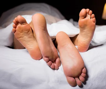 Two pairs of feet sticking out from under white bed covers, symbolizing intimacy and connection.