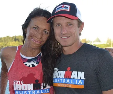 Two people smiling, both wearing 2016 Ironman Australia shirts, with greenery in the background.
