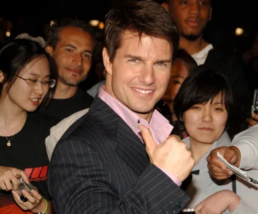 Tom Cruise smiling and giving a thumbs-up surrounded by fans at an event.