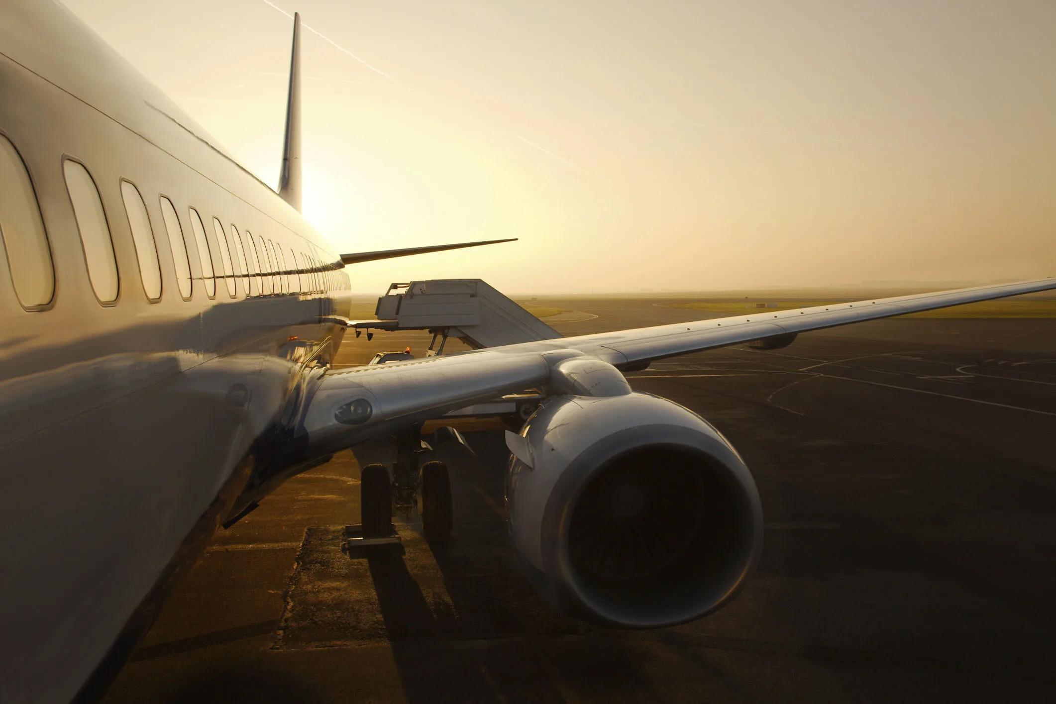 Aircraft on the tarmac at sunset with boarding stairs attached.

