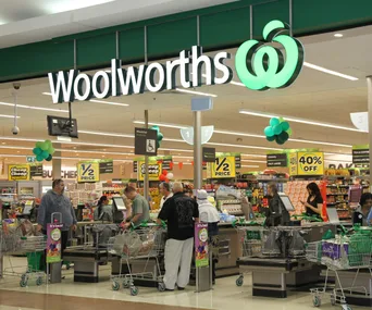 "Woolworths supermarket interior with customers at checkout, featuring sale signs and green decor."