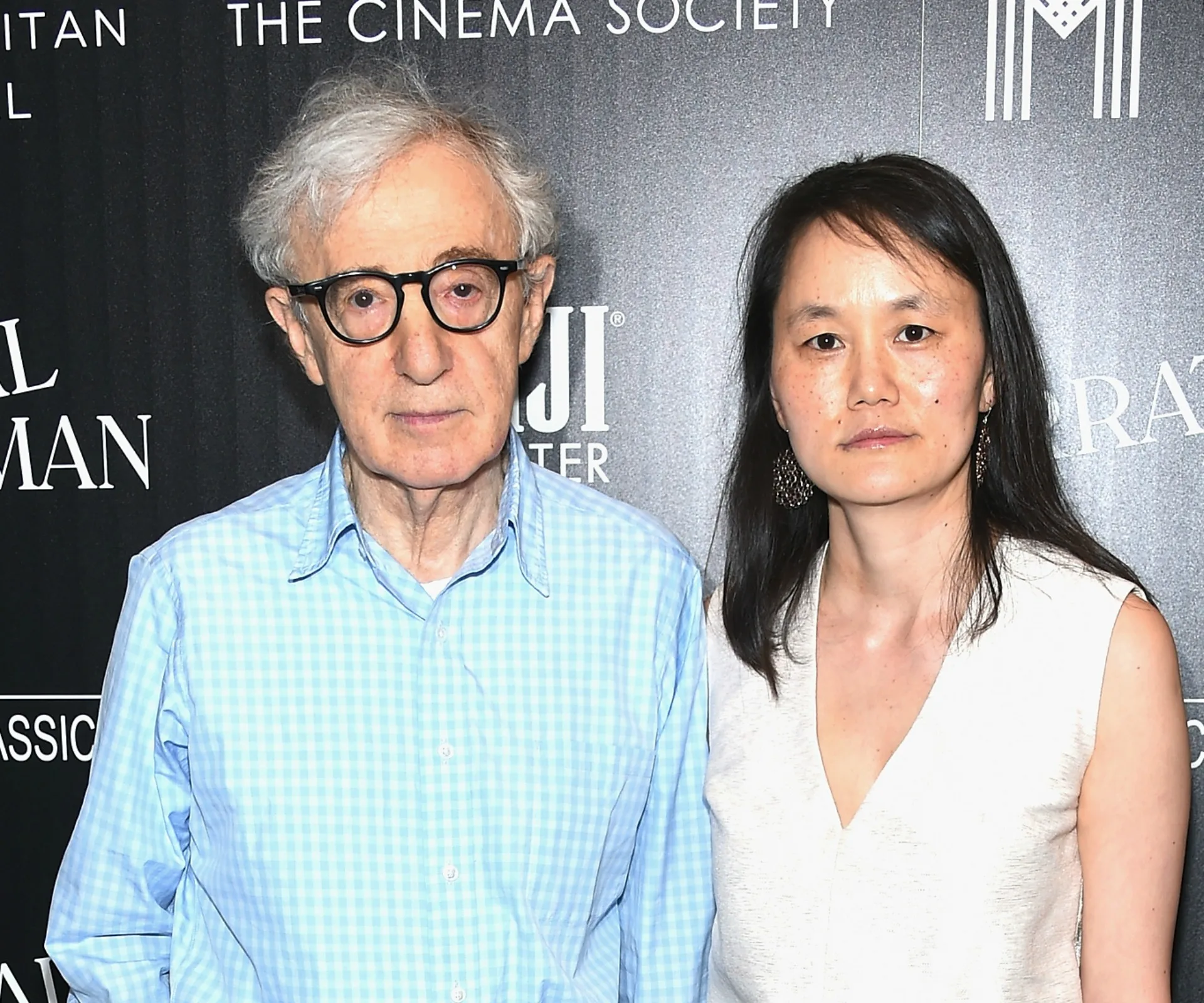 A man in glasses and a woman pose together at a Cinema Society event, standing in front of a branded backdrop.
