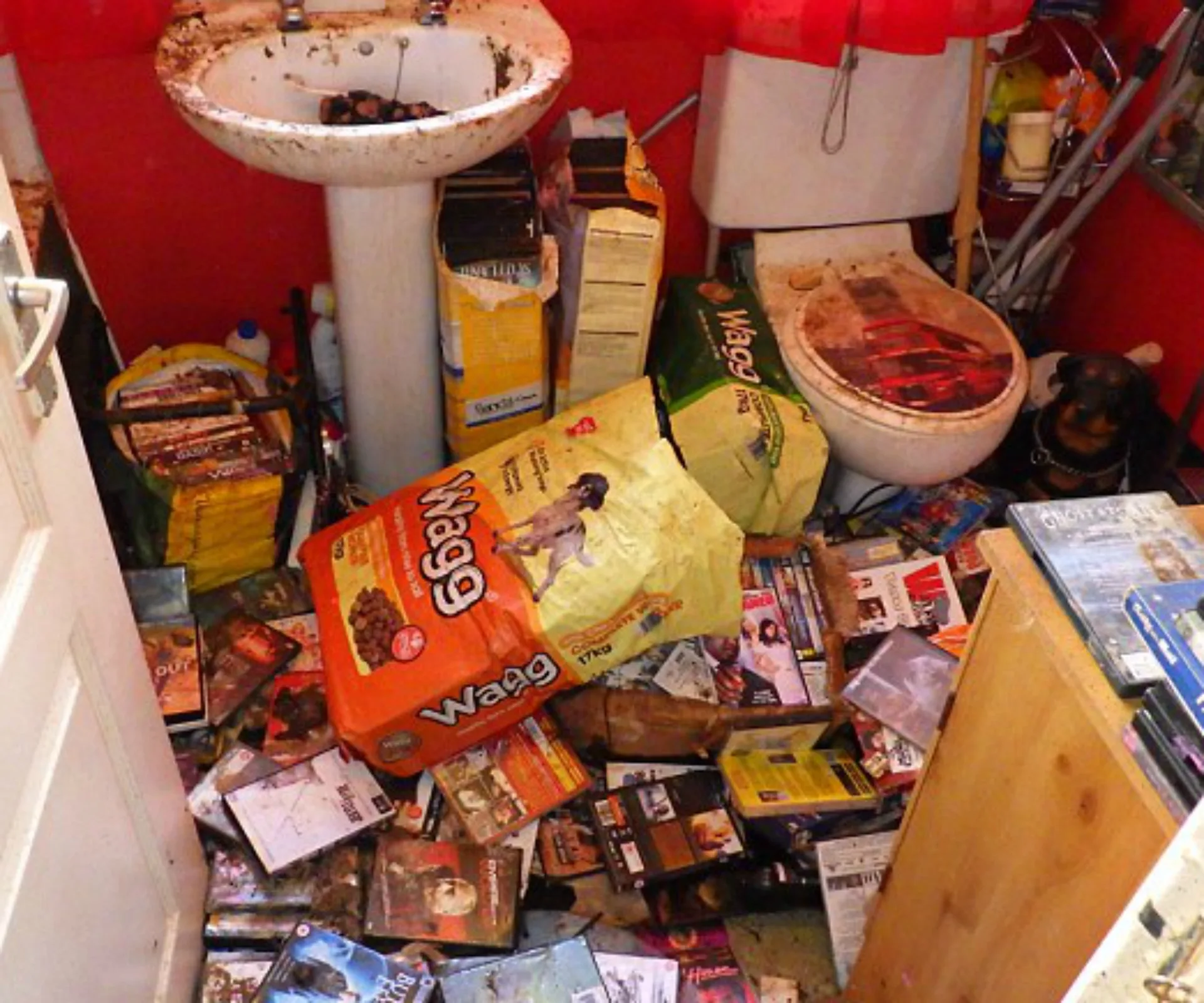 Cluttered bathroom with dog food bags, scattered DVDs, and dirty fixtures.
