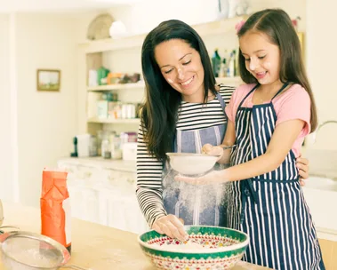 Mother and daughter baking together, smiling with flour on their faces, in a cozy kitchen setting.