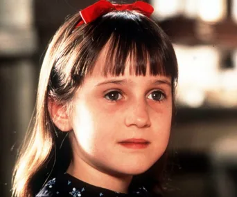 Young girl with brown hair and red ribbon, wearing a floral dress, from the movie "Matilda."