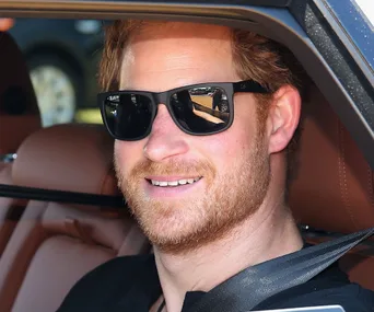 A man with red hair and sunglasses smiling while seated in a car.