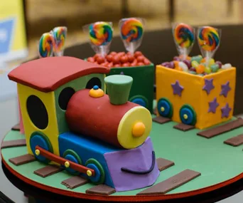 Colorful train cake with candy-filled cars, decorated with stars and circular windows, on a track-shaped base.