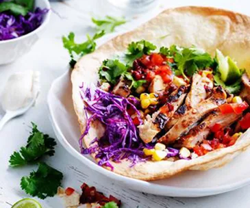 Grilled chicken taco with purple cabbage, corn, tomatoes, and cilantro in a tortilla shell.