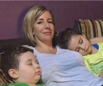 A woman sitting with two children asleep on her, all relaxed on a couch.