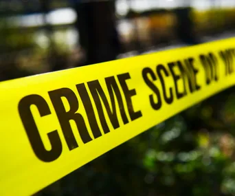 Yellow "CRIME SCENE DO NOT CROSS" tape stretches across a blurred outdoor background.