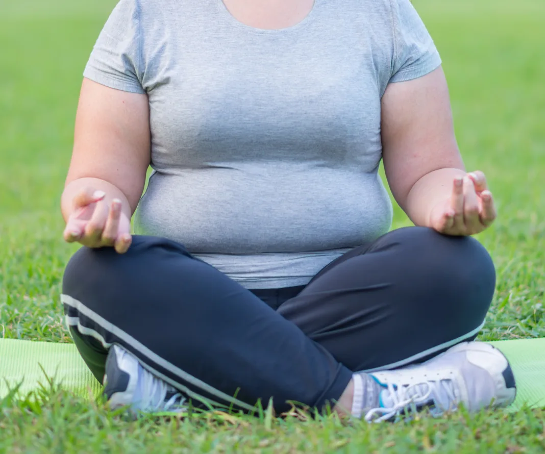 Person meditating on grass in a seated position, wearing a gray shirt and black pants.