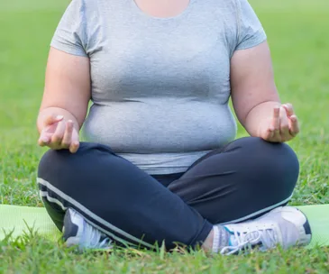 Person meditating on grass in a seated position, wearing a gray shirt and black pants.