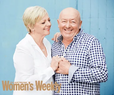 Elderly couple smiling and holding hands against a blue background.