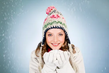 Woman in winter clothes holding snow, smiling under falling snowflakes.