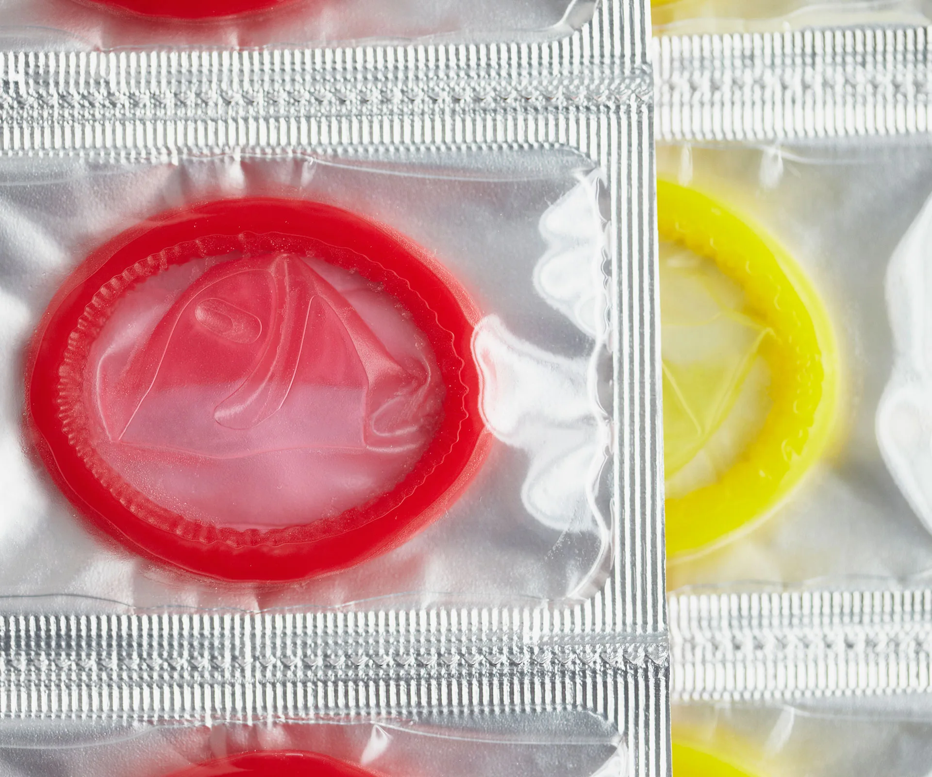Close-up of packaged red and yellow condoms in silver foil wrappers.