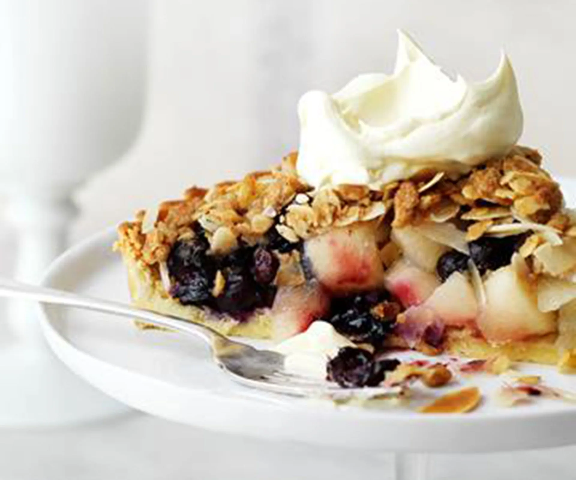 A slice of apple-blueberry pie with a crumb topping and whipped cream on a white plate.