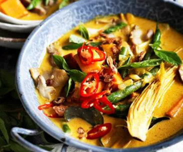 A bowl of vibrant Thai curry with vegetables, red chilies, and herbs in creamy coconut broth.