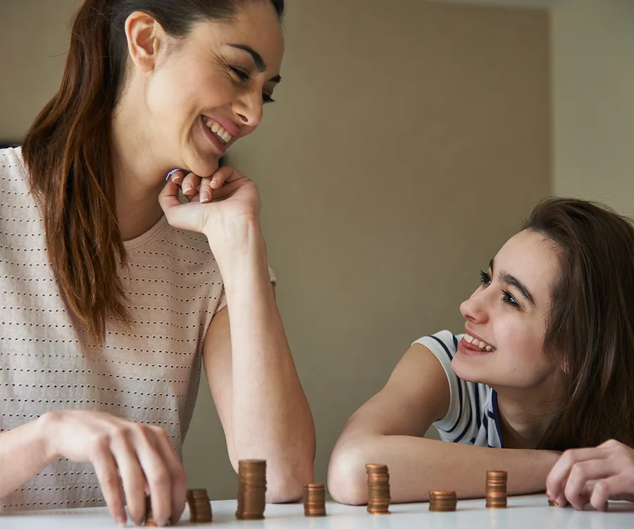 Mother and daughter smiling at each other with stacks of coins on the table.