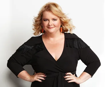 Magda Szubanski in a black dress with tassels on shoulders, smiling with hands on hips.