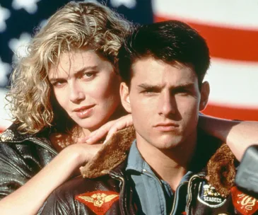 Actors in leather jackets from "Top Gun" pose in front of an American flag.