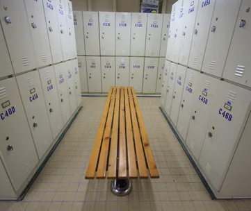 Locker room with white lockers and a wooden bench in the center.