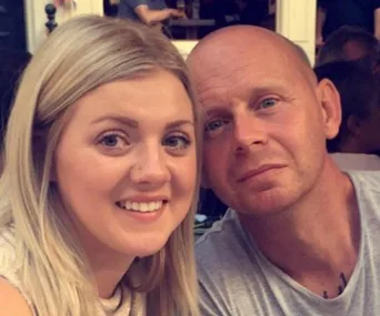 A couple smiling at the camera in a casual outdoor setting.