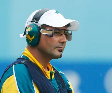 Shooter wearing protective gear and uniform, focused on a target at a sporting event.