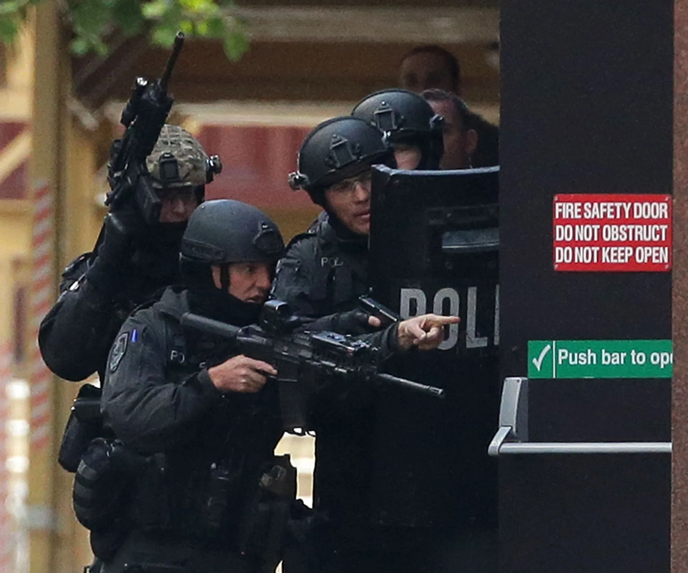 SWAT team members in tactical gear, holding rifles and a shield, standing by a fire safety door during an operation.