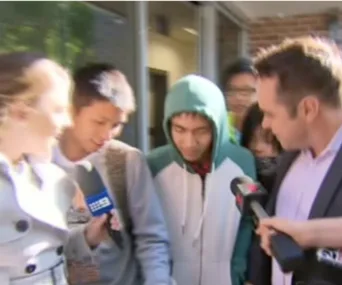Group of people exiting a building, some with microphones, including one wearing a green hoodie.