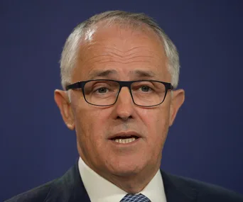 A person in glasses speaking at a public event or press conference.