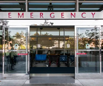 Entrance to an emergency room with glass doors and wheelchairs visible inside.