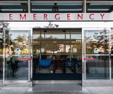 Entrance to an emergency room with glass doors and wheelchairs visible inside.