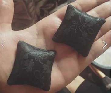 Hand holding two tiny black pillows with a floral pattern.