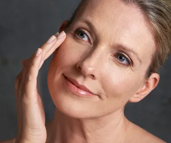 Woman gently touching her cheek, showcasing skincare routine.