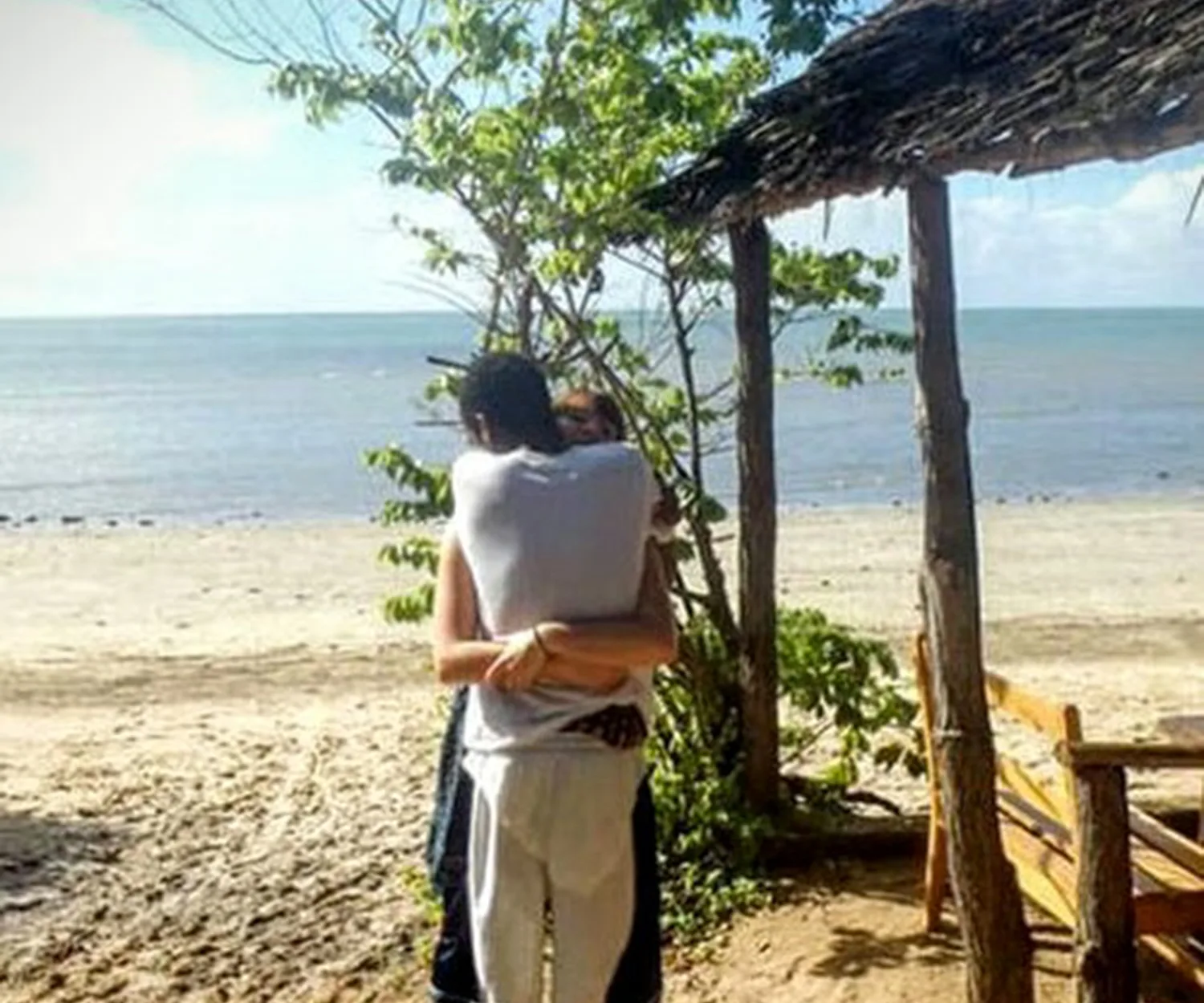 Two people hugging on a beach; the optical illusion makes their legs appear misaligned, creating confusion.
