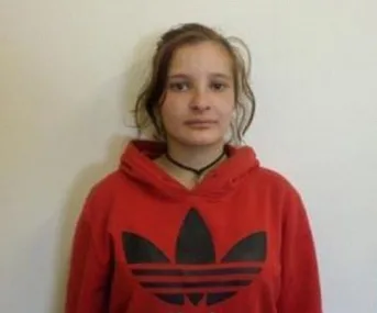Young woman in red hoodie with black logo, straight hair, neutral expression, standing against plain background.