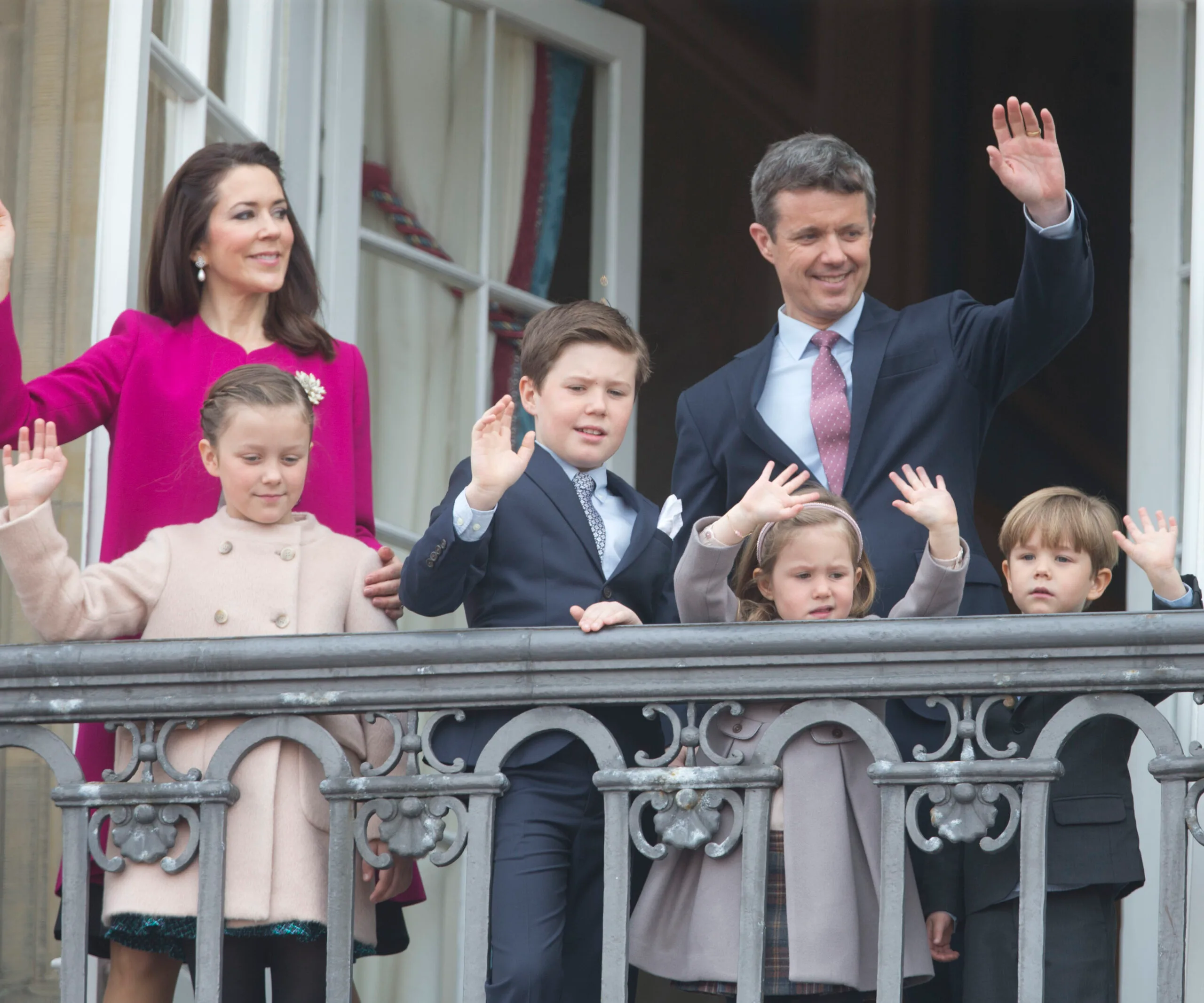 Royal family on balcony waving to crowd.