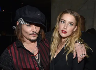 Two people posing closely at an event, one wearing a black cap and striped shirt, the other with blonde hair and red lips.