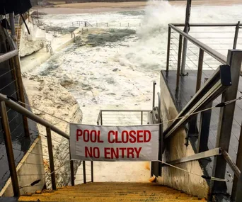 Pool staircase overlooking rough sea waves, with a "Pool Closed No Entry" sign across the entrance.