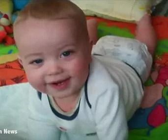 A smiling baby in a white outfit lies on a colorful play mat, looking towards the camera.