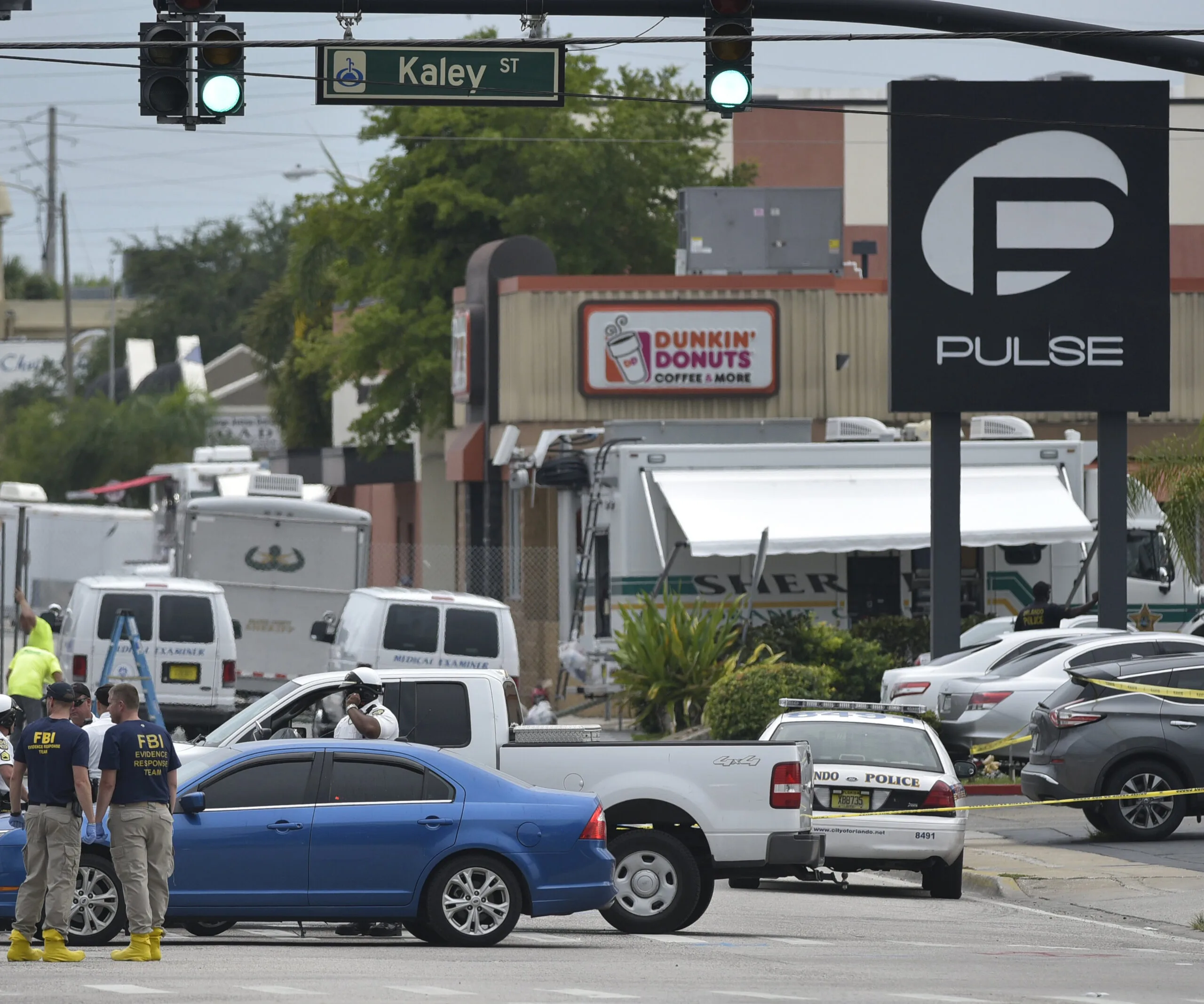 FBI and police investigate outside Pulse nightclub in Orlando, with visible emergency vehicles and a Dunkin' Donuts in the background.