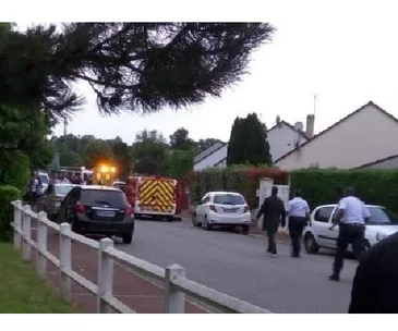 Police vehicles and officers surround a residential street, emergency lights flashing in the evening.