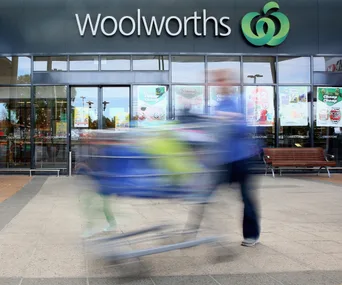 Blurred person pushing a shopping cart outside Woolworths storefront.