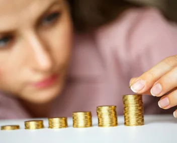 A person stacking gold coins into a pyramid, illustrating savings and financial growth.