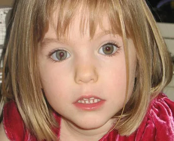 A young girl with short blonde hair and a red dress looking at the camera.