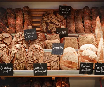 Various types of bread displayed on shelves with German labels in a bakery.