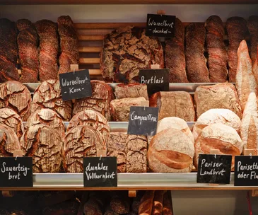 Various types of bread displayed on shelves with German labels in a bakery.