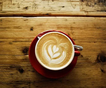 A red cup of coffee with latte art on a wooden table.